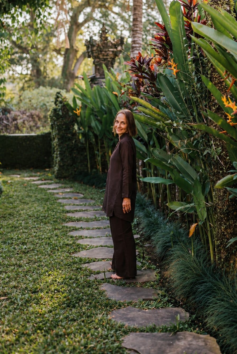 Christiane in Braun auf einem Gartenweg zwischen tropischen Pflanzen.